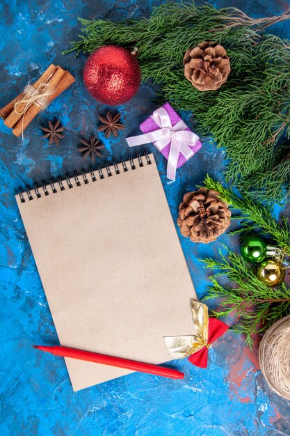 Top view a notebook pine tree branches cones cinnamon anises red pencil on blue background