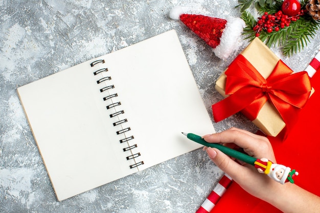 Top view notebook small santa hat present green pen in female hand on grey white table