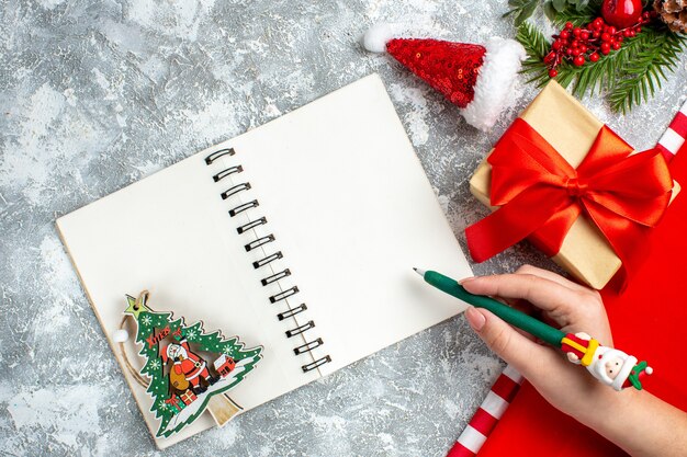 Top view notebook small santa hat present green pen in woman hand on grey white table