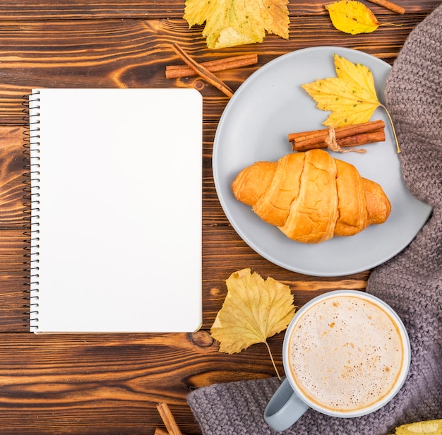 Top view notebook surrounded by coffee and croissant