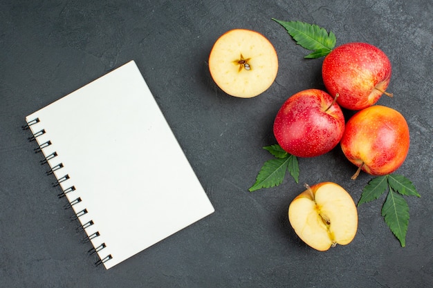 Top view of notebook and whole cut fresh red apples and leaves on black background