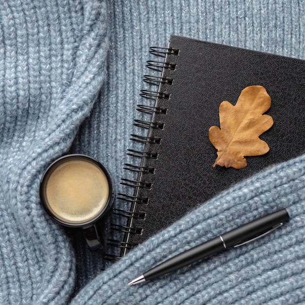 Free photo top view of notebook with autumn leaf and cup of coffee on sweater