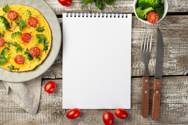 Top view of notebook with breakfast omelette and tomatoes