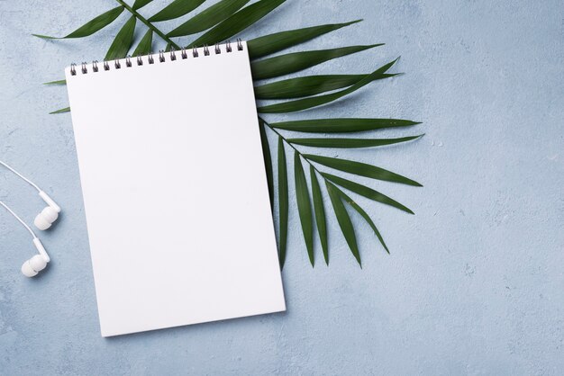 Top view of notebook with headphones and leaves on desk