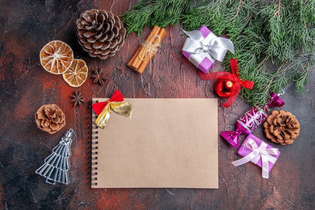 Top view a notebook with little bow pine tree branches with cones and xmas tree toys cinnamon dried lemon slices anises on dark red background