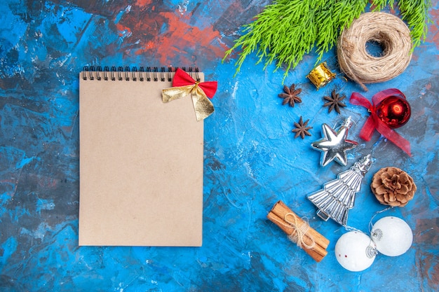 Top view a notebook with little bow straw thread xmas tree toys anise seeds cinnamon sticks on blue-red background