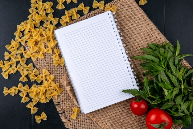 Foto gratuita vista dall'alto del taccuino con pomodori pasta cruda e un mazzo di menta su un tovagliolo beige