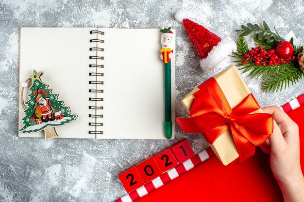 Top view notebook wood blocks small santa hat present in female hand pencil on grey white table