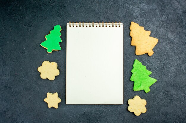 Top view notebook xmas cookies on dark surface