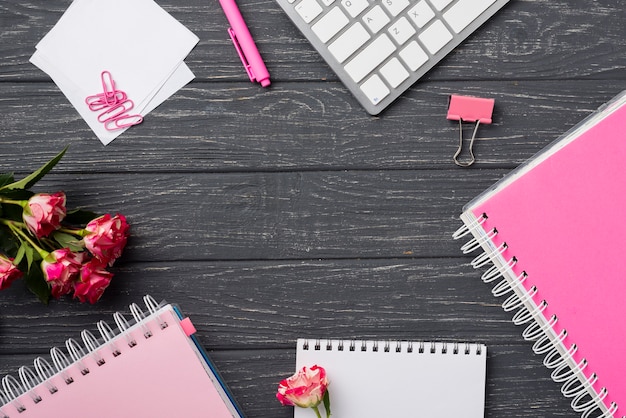 Top view of notebooks on wooden desk with bouquet of roses and paper clips