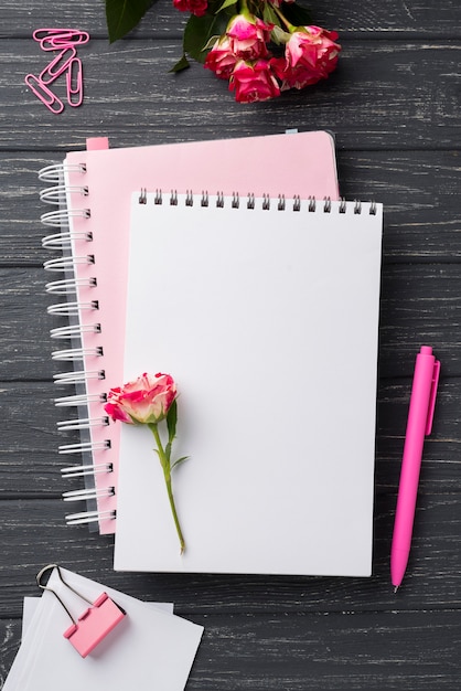 Top view of notebooks on wooden desk with bouquet of roses and pen