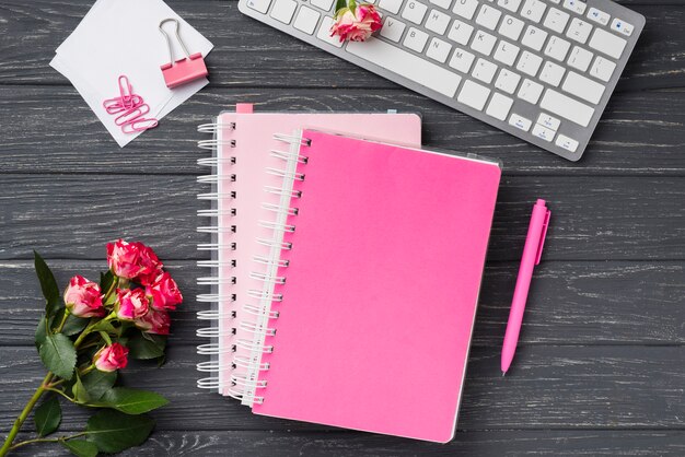 Top view of notebooks on wooden desk with bouquet of roses and sticky notes