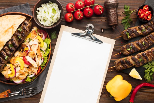 Top view of notepad with delicious kebabs and vegetables