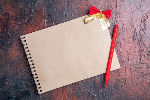 Top view a notepad with small bow red pen on dark red background with copy space