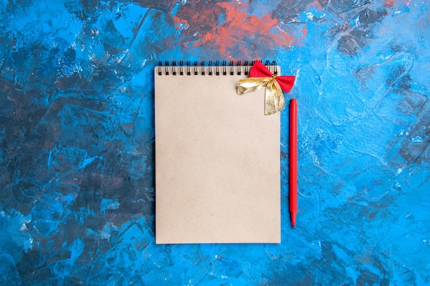 Top view a notepad with small bow red pencil on blue background with copy space