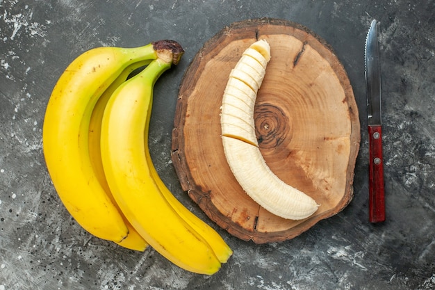 Top view nutrition source fresh bananas bundle and chopped on wooden cutting board knife on gray background