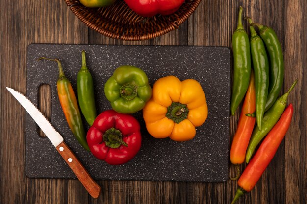 Top view of nutritional peppers on a black kitchen board with knife with peppers isolated on a wooden surface