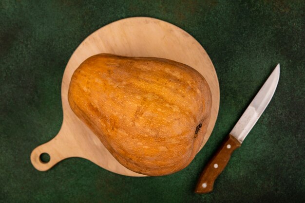 Top view of a nutritious orange vegetable pumpkin isolated on a wooden kitchen board with knife on a green wall