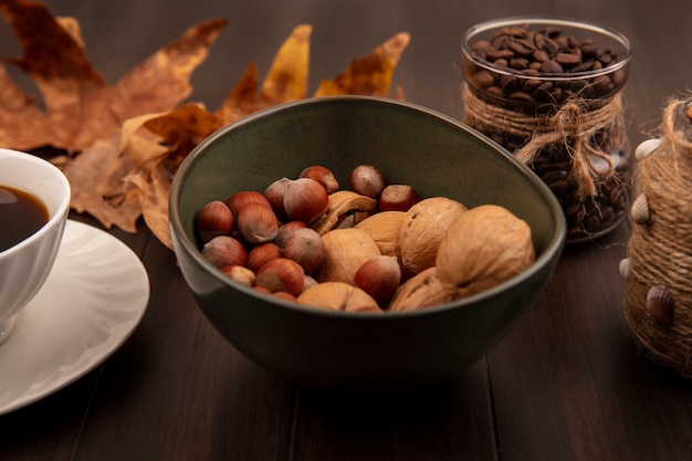 Top view of nuts on a bowl with coffee beans on a glass jar with a cup of coffee on a wooden surface