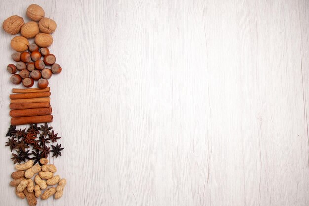 Top view nuts and cinnamon cinnamon sticks peanuts walnuts hazelnuts on the left side of the white table