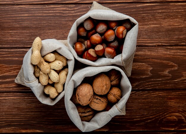 Top view of nuts in sacks walnuts peanuts and hazelnuts in shell on wooden background