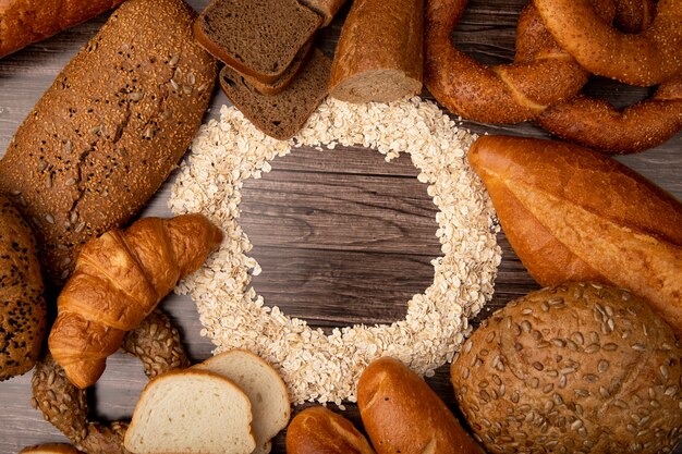 Top view of oat-flakes set in circular shape and breads around as baguette rye white cob bagel on wooden background with copy space