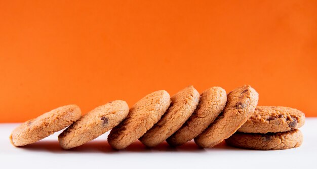 Вид сверху овсяное печенье с шоколадом на бело-оранжевом фоне
