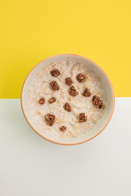 Top view of oatmeal with milk and walnut in bowl on white and yellow background