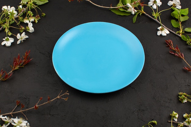 top view ocean blue plate around white flowers on the dark floor