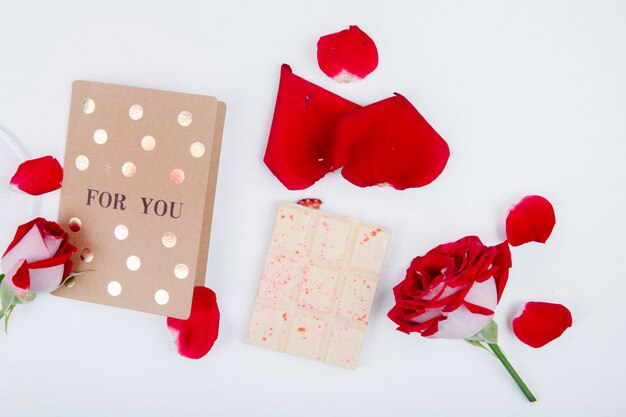 Top view od red rose with small postcard and white chocolate with red rose petals on white background