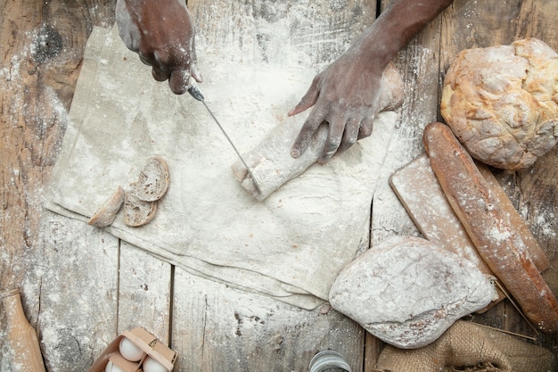 Вид сверху афро-американский мужчина готовит свежие хлопья, хлеб, отруби на деревянном столе. вкусная еда, питание, крафтовый продукт