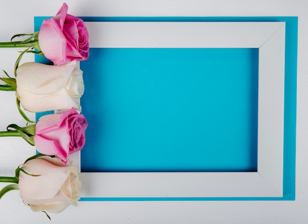 Бесплатное фото Вид сверху пустой рамки с белыми и розовыми розами на синем фоне с копией пространства