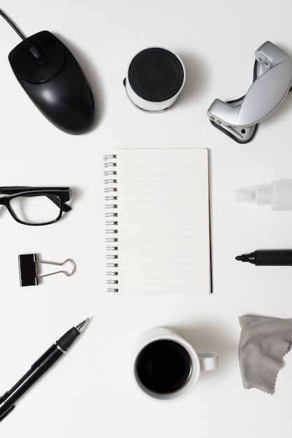 無料写真 文房具と空白のスパイラルメモ帳の平面図。コーヒーカップ;白い机の上の眼鏡