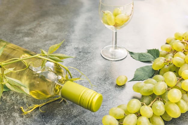 Вид сверху бутылки белого вина, зеленого вина, бокала и спелого винограда на старинных серых каменных фонах стола ...