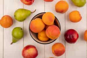 無料写真 木製の背景にアプリコットのボウルと桃アプリコットと梨として果物のパターンの平面図