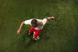 Бесплатное фото Вид сверху кавказского футболиста или футболиста на зеленом фоне травы. тренировка юных моделей, тренируется. удар по мячу, атака, ловля. понятие спорта, соревнования, победы.
