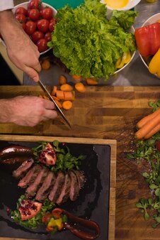 야채 장식으로 쇠고기 스테이크를 준비하는 호텔 또는 레스토랑 주방에서 요리사의 손