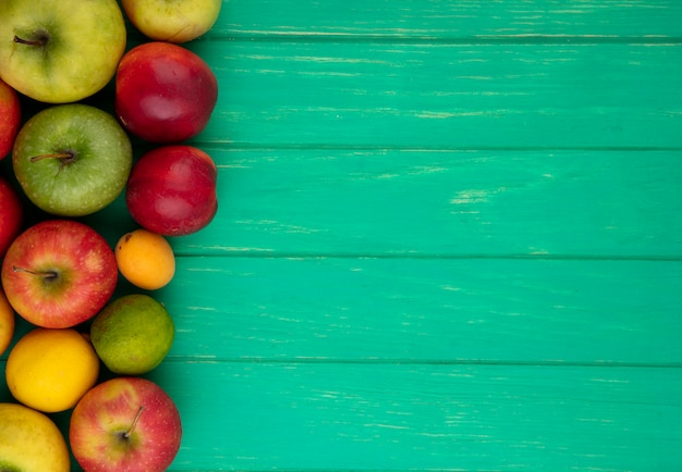 Бесплатное фото Вид сверху цветных яблок с персиками, лимоном и лаймом на зеленой поверхности