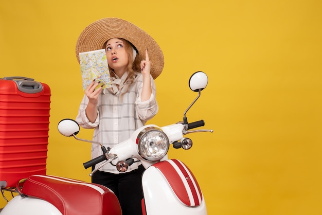 バイクに座って地図を上向きに保持している彼女の荷物を収集する帽子をかぶって自信を持って若い女性の上面図