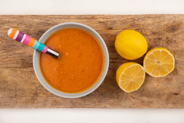 白い背景の上のレモンとスプーンで木製のキッチンボードのボウルにおいしいレンズ豆のスープの上面図