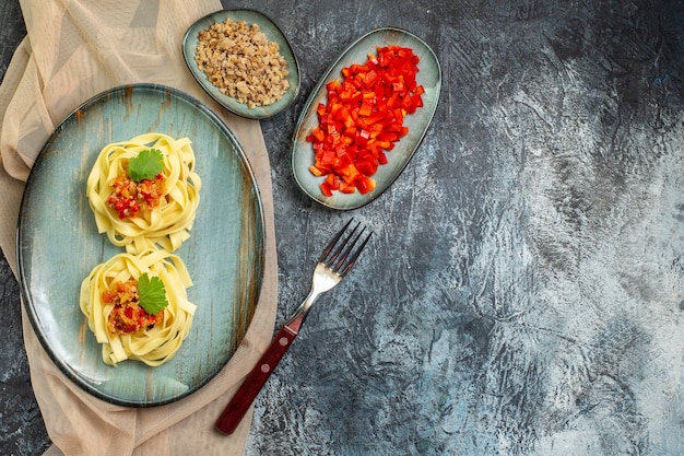 Бесплатное фото Вид сверху вкусной пасты на синей тарелке, подаваемой с помидорами и мясом на ужин на коричневом полотенце, его ингредиенты