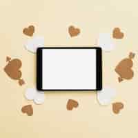 Бесплатное фото Вид сверху цифрового планшета с белой и золотой сердечной этикеткой на бежевой поверхности