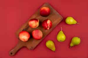 無料写真 赤い背景の上の梨と木製キッチンボード上の新鮮でジューシーな桃のトップビュー