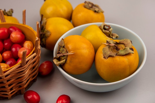 Бесплатное фото Вид сверху свежих фруктов хурмы на миске с плодами сердолика на ведре на серой поверхности