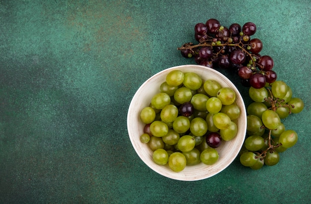 Бесплатное фото Вид сверху виноградных ягод в миске и винограда на зеленом фоне с копией пространства