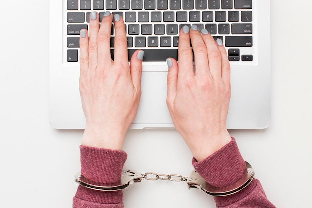 Бесплатное фото Вид сверху руки с наручниками работает на ноутбуке