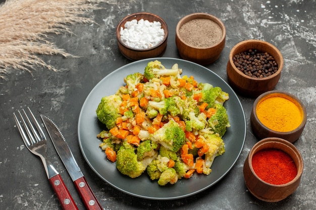 Бесплатное фото Вид сверху здоровой еды с брокколи и морковью на черной тарелке и специями с вилкой и ножом