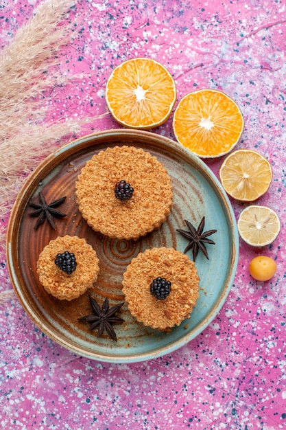Бесплатное фото Вид сверху маленьких вкусных пирожных с дольками апельсина на розовой поверхности
