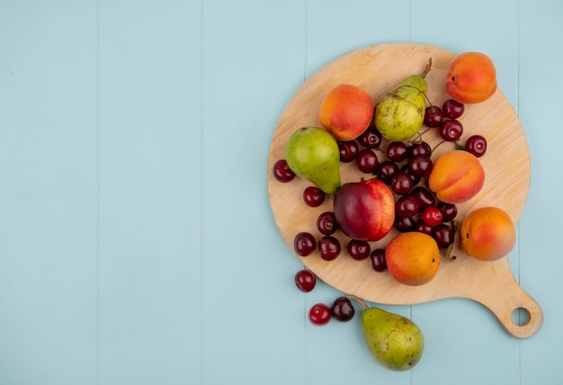 Бесплатное фото Вид сверху на узор из фруктов в виде персика, груши, абрикоса, вишни на разделочной доске и на синем фоне с копией пространства