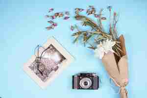 Бесплатное фото Вид сверху фото старой камеры с белым цветком хризантемы в крафт-бумаге и сухих бутонах роз, разбросанных по синему